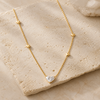A delicate gold necklace with small heart-shaped charms and a heart-shaped clear gemstone pendant, displayed on a textured beige stone slab.