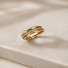 A gold ring with a channel-set row of small clear stones, displayed on a light beige stone surface.