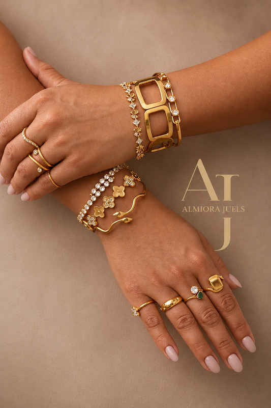 Elegant close-up of luxury gold bracelets and rings styled on crossed hands against a soft neutral beige background, featuring demi-fine jewellery with sparkling stone details by Almiora Juels.