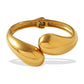 A polished gold-tone metal cuff bracelet with a unique organic, rounded teardrop-like design, shown on a clean white background with a soft shadow.