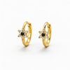 A pair of gold huggie hoop earrings with a star-shaped floral center, featuring a small black round stone surrounded by clear stones, set against a plain white background.